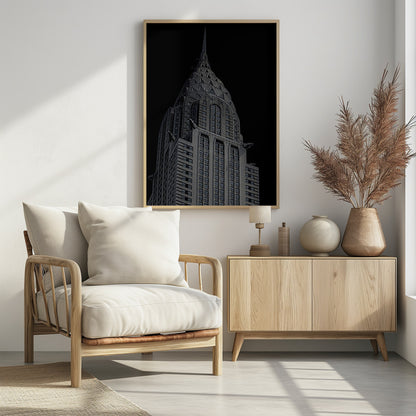 A dramatic, low-angle, black and white photograph of the top of the Chrysler Building, showcasing its iconic Art Deco spire and architectural details against a solid black background. Decor