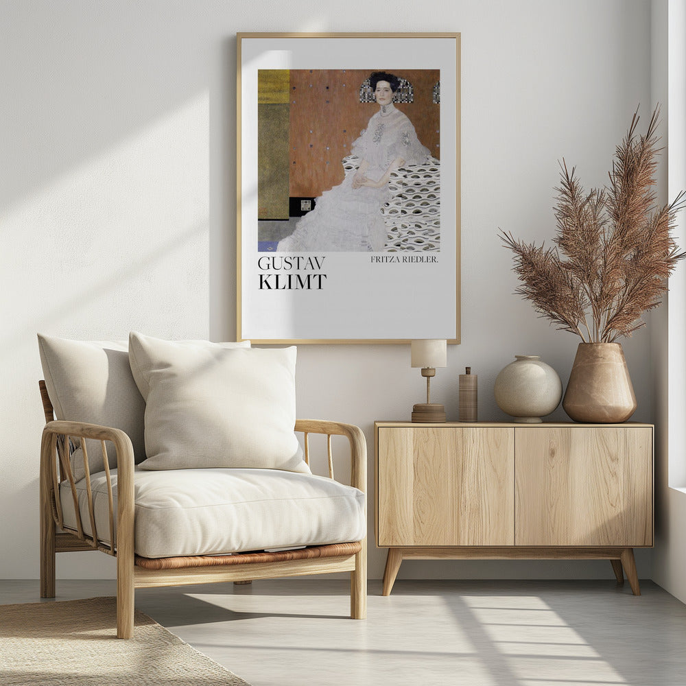 A framed art print of Gustav Klimt's 1906 painting, 'Portrait of Fritza Riedler'. A woman with dark, upswept hair wearing a detailed, high-necked white gown sits in a patterned chair against a warm, textured brown and gold background. Below the artwork, on a white border, the text 'GUSTAV KLIMT' and 'FRITZA RIEDLER.' is printed. Print