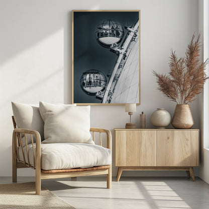A dramatic low-angle, black and white photograph of two spherical glass pods of the London Eye Ferris wheel. Silhouettes of people are visible inside the pods against a dark, solid sky, with the massive white structure of the wheel on the right. Print