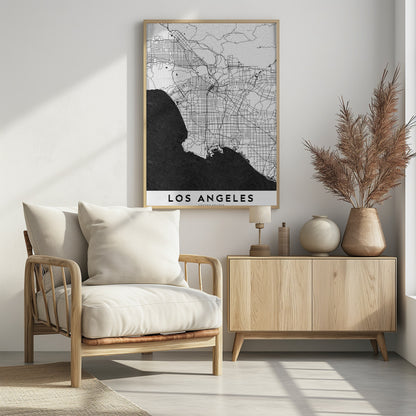 A minimalist black and white framed poster of a street map of Los Angeles. The land is white with an intricate grid of black lines representing roads and highways, while the Pacific Ocean is a solid, textured black. A white band at the bottom contains the city's name, 'LOS ANGELES', in a bold, black sans-serif font. Decor