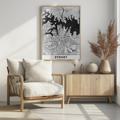 A modern black and white framed art print of a city map of Sydney, Australia. The water bodies are shown in solid textured black, while the land is depicted with a detailed white street grid. At the bottom, the word 'SYDNEY' is printed in bold capital letters. Poster