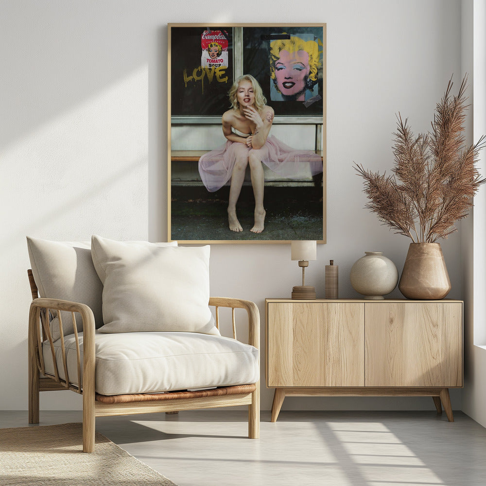 A blonde woman styled like Marilyn Monroe sits on a bench, wearing a pink tulle skirt. Behind her, a dark window features an Andy Warhol-style poster of Monroe, a Campbell's soup can parody, and the word 'LOVE' in gold graffiti. Artwork