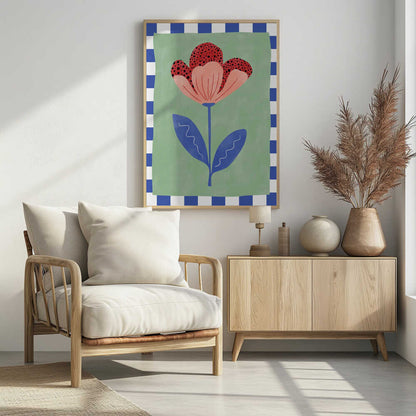 A framed illustration of a stylized flower with red polka-dotted and pink petals. The flower has a blue stem and two blue leaves, set against a sage green background with a blue and white checkered border. Artwork
