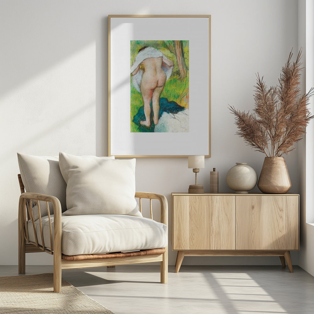 A framed pastel artwork by Edgar Degas showing the back of a nude woman as she dries herself with a white towel in a lush green landscape. The impressionist style is evident in the soft, textured application of color. Artwork