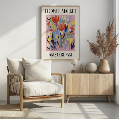 A vintage-style poster for the 'FLOWER MARKET AMSTERDAM'. The artwork features a vibrant illustration of various stylized flowers, including red tulips, white daisies, and yellow and blue foliage, set against a solid pink background. The text is in a black serif font, with 'FLOWER MARKET' at the top and 'AMSTERDAM' at the bottom, all enclosed by a cream-colored border and a simple black frame. Poster