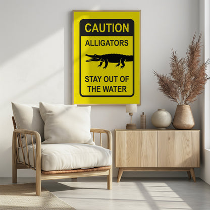 A yellow and black rectangular warning sign in a black frame. The sign reads 'CAUTION ALLIGATORS' at the top, features a black silhouette of an alligator in the center, and says 'STAY OUT OF THE WATER' at the bottom. Decor