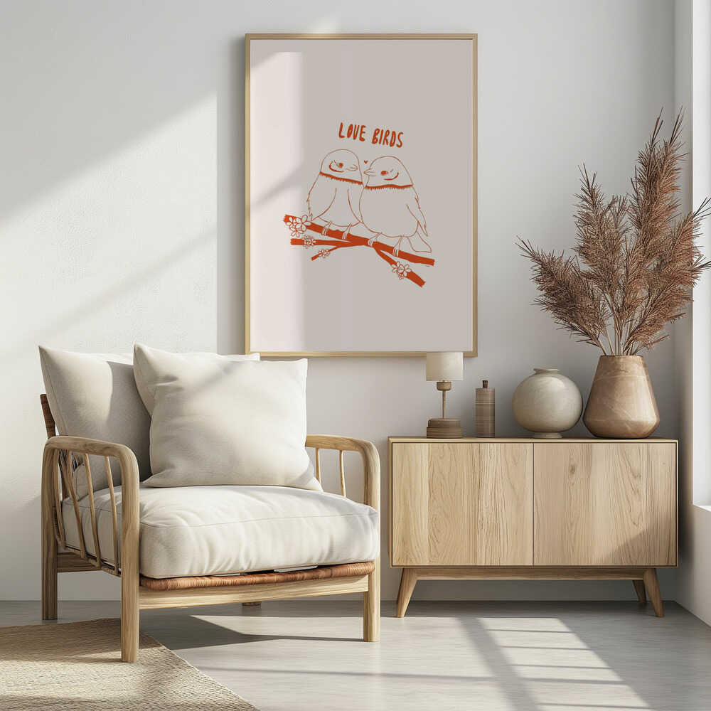 A framed art print featuring a minimalist, reddish-orange illustration on a cream background. Two cartoonish, plump birds sit close together on a flowering branch, looking at each other affectionately. Above them, the text 'LOVE BIRDS' is written in a playful, rounded font. Decor