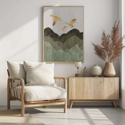 A minimalist art print of three golden bird silhouettes flying over a stylized landscape of layered mountains in muted shades of green and brown, set against a light grey, textured sky and enclosed in a thin black frame. Print