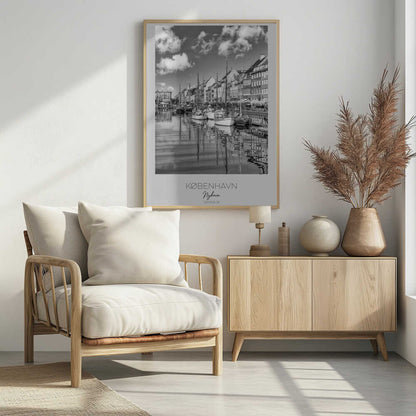 A black and white poster of Nyhavn harbor in Copenhagen. The photograph shows traditional sailboats and ships moored along a canal, with a line of historic, multi-story buildings on the far bank. The sky has fluffy clouds, and the entire scene is reflected in the calm water. The poster has a white border with the text 'KØBENHAVN', 'Nyhavn', and 'DANMARK' at the bottom, and is shown within a black frame. Poster