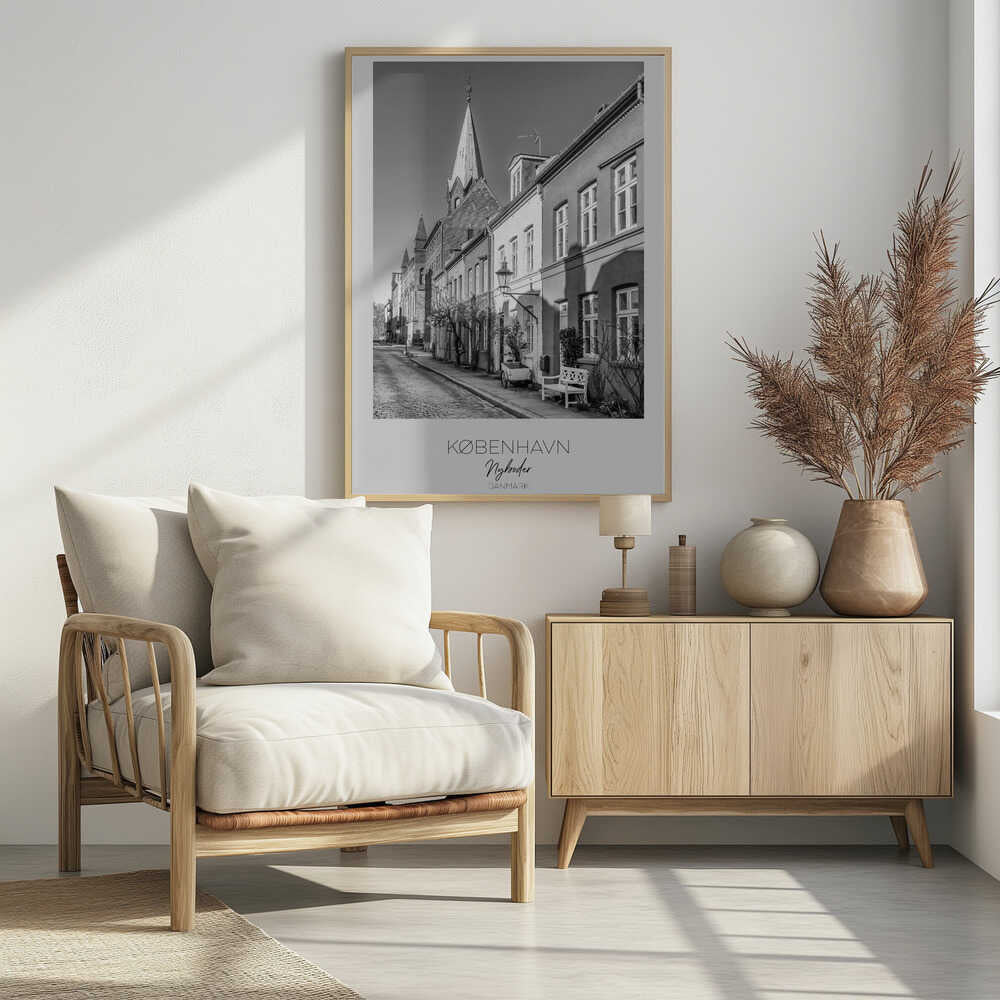 A black and white framed travel poster of a charming cobblestone street in Nyboder, Copenhagen. The photograph shows a sunlit row of historic houses with a prominent church steeple in the background. At the bottom of the poster, the words 'KØBENHAVN', 'Nyboder', and 'DANMARK' are written. Wall Art