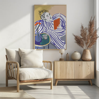 A stylized, framed illustration of a person with dark hair in a messy bun, wearing a blue and white striped top, reclining comfortably while engrossed in an orange book. Beside them is a small table with a blue vase holding three orange flowers and a black and white striped mug. The background is a soft beige color. Print