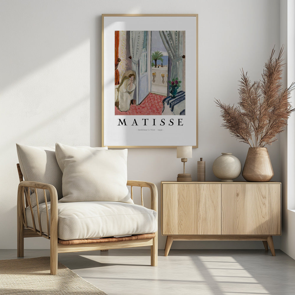 A framed art print of Henri Matisse's painting 'Intérieur à Nice - 1939'. The painting depicts a woman in a white robe sitting in a sunlit room with an open door leading to a balcony overlooking the sea and a palm tree. The poster has a white border with the artist's name and the title below the artwork. Artwork