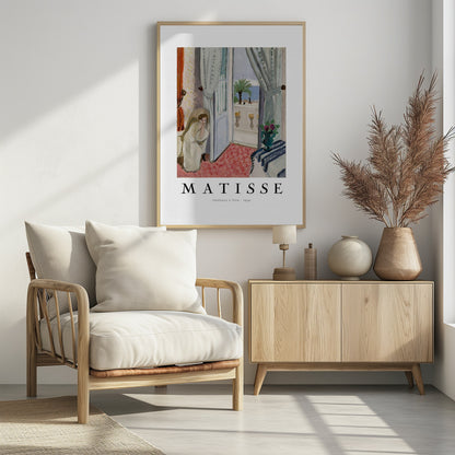 A framed art print of Henri Matisse's painting 'Intérieur à Nice - 1939'. The painting depicts a woman in a white robe sitting in a sunlit room with an open door leading to a balcony overlooking the sea and a palm tree. The poster has a white border with the artist's name and the title below the artwork. Artwork
