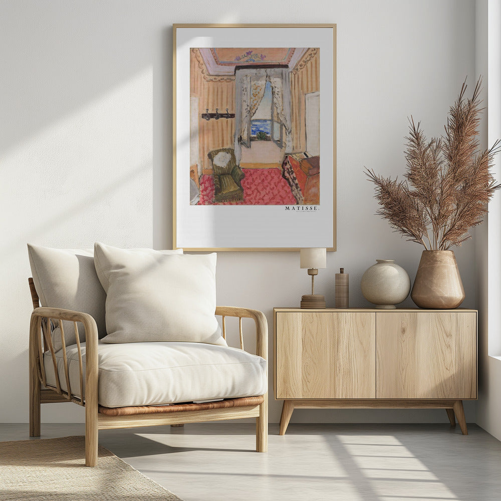 A framed print of a painting by Henri Matisse. The artwork depicts an interior room scene with peach-colored walls, a vibrant pink and red patterned rug, and an armchair. An open window with lace curtains offers a view of the blue sea. Decor