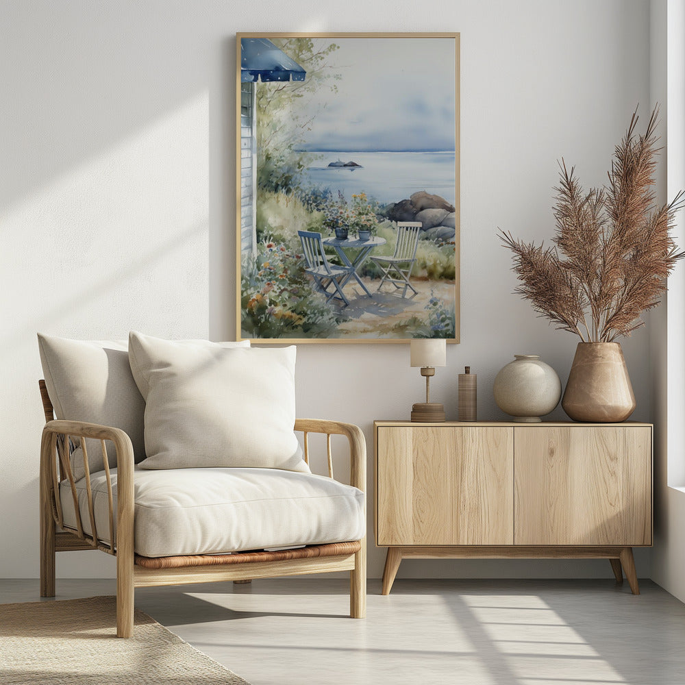 A watercolor painting of a tranquil coastal scene. A light blue bistro table and two matching chairs sit in a lush garden filled with flowers, overlooking a calm body of water. In the distance, a small island is visible under a soft, hazy sky. Part of a house with a blue awning can be seen on the left. Print