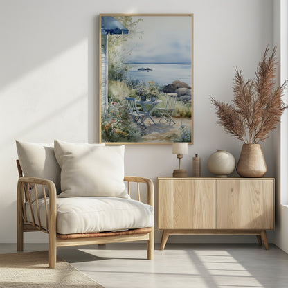 A watercolor painting of a tranquil coastal scene. A light blue bistro table and two matching chairs sit in a lush garden filled with flowers, overlooking a calm body of water. In the distance, a small island is visible under a soft, hazy sky. Part of a house with a blue awning can be seen on the left. Print