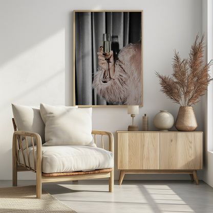 A close-up photograph of a woman's hand with black nail polish holding a tall, elegant flute of champagne. She is wearing a soft, shaggy pink faux fur coat, with a silver-gray curtain in the background, creating a luxurious and celebratory mood. Print