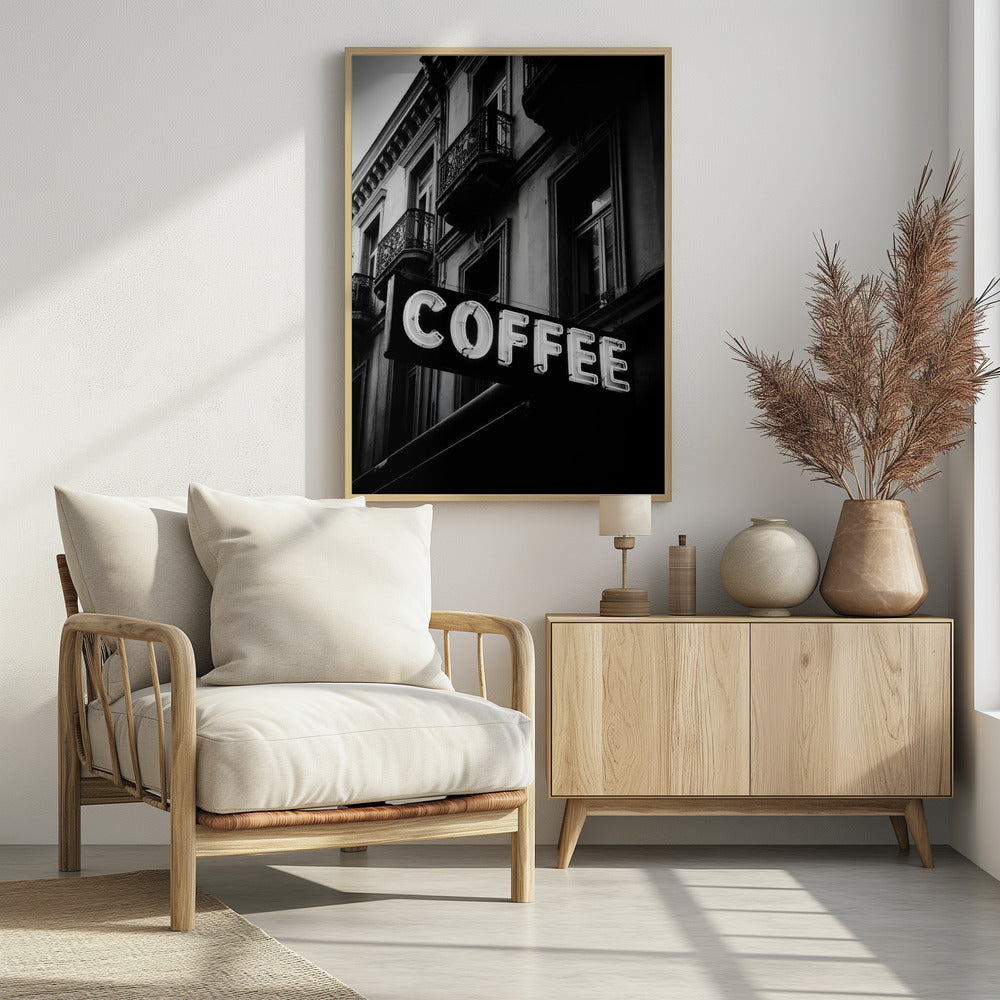 A dramatic, low-angle, black and white photograph of a bright white neon sign that reads 'COFFEE', mounted on a classic-style building with ornate balconies. Print