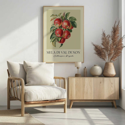 A vintage-style botanical poster featuring a realistic illustration of a cluster of red apples on a branch against a pale yellow-green background. Below the image is the text 'MELA DI VAL DI NON' in a serif font and 'Coltivazioni Pregiate' in a cursive script. The artwork is enclosed in a black frame. Print
