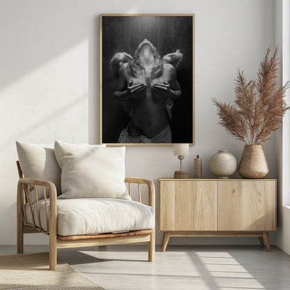 A dramatic black and white photograph of a topless woman with angel wings, her head tilted back towards a light from above. She is covering her breasts with her hands, and a white cloth is draped around her hips. Poster