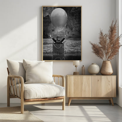 A whimsical black and white photograph of a young girl wearing an aviator cap and goggles, joyfully raising her arms in the air while standing in a wicker basket attached to a large balloon, mimicking a hot air balloon. The scene is set by the water with a stone wall in the background. Poster