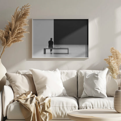 A black and white photograph of a person seen from behind, sitting alone on a wooden bench in a minimalist art gallery. They face a large, starkly divided wall, half white and half black. The scene is presented within a silver picture frame. Poster