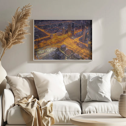 A stunning aerial view of a futuristic city at night, with brilliantly lit highways forming intricate patterns of golden light amidst towering skyscrapers, enclosed in a silver frame. Poster