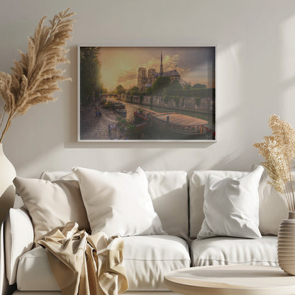 A scenic photograph of the Notre Dame Cathedral in Paris during a warm, golden sunset, as viewed from across the River Seine. People are strolling along the cobblestone riverbank and riding on tour boats docked on the water. The image is presented within a silver picture frame. Decor