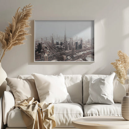 An aerial photograph of a sprawling modern cityscape on a hazy day, framed in silver. The iconic Burj Khalifa stands tall in the center background, surrounded by numerous other skyscrapers and a complex network of highways and interchanges in the foreground, all rendered in a muted, slightly sepia-toned color palette. Print