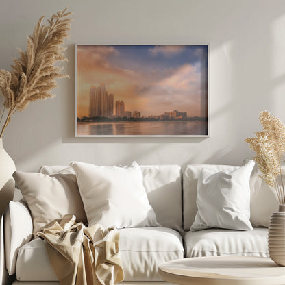 A framed photograph of the Abu Dhabi city skyline at sunset, featuring modern skyscrapers and the Emirates Palace hotel glowing in warm, orange light. The buildings are reflected in the calm water of the foreground, under a sky with soft orange and blue clouds. Poster