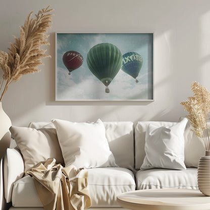 A low-angle photograph of three colorful hot air balloons floating in a cloudy blue sky, presented in a silver frame. A large green balloon is in the center, with a red balloon on the left and a dark blue balloon on the right, all featuring logos. Wall Art