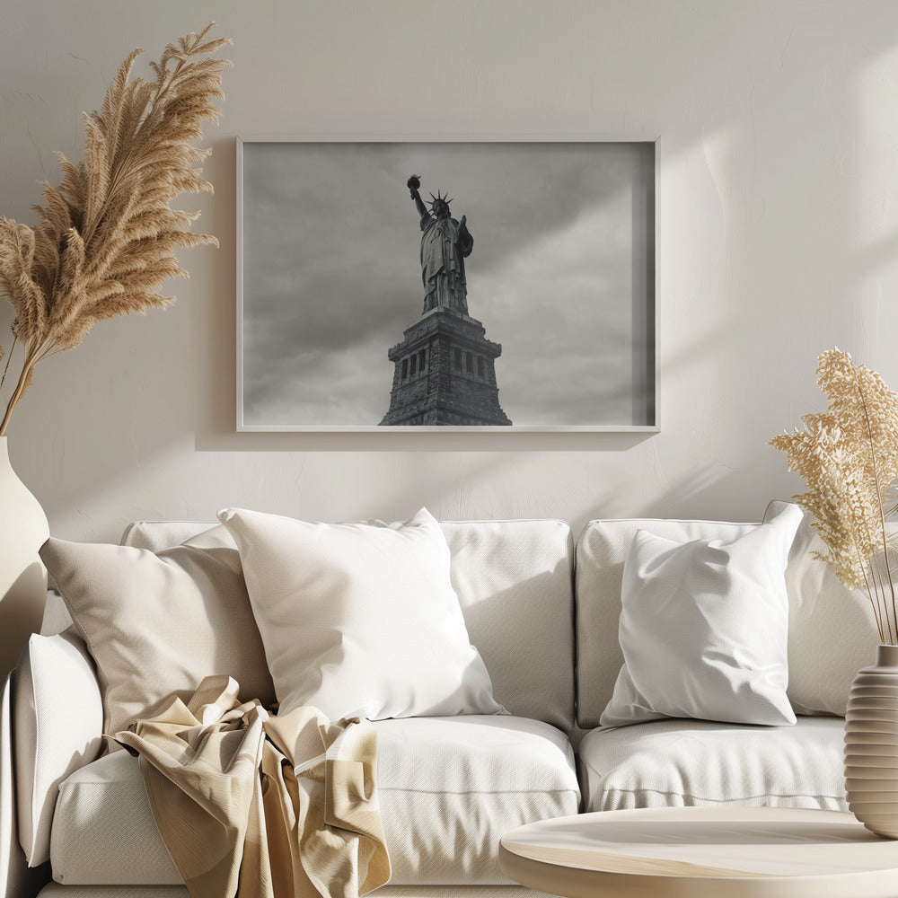 A low-angle, black and white photograph of the Statue of Liberty standing tall against a cloudy, dramatic sky, enclosed in a silver frame. Poster