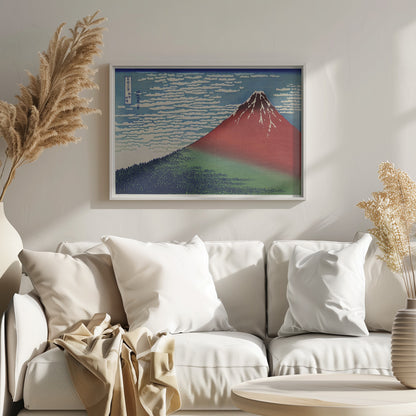 A Japanese woodblock print, Hokusai's 'Fine Wind, Clear Morning', showing a large, reddish-brown Mount Fuji with snow at its peak. Below the mountain is a dense green forest, and above is a blue sky with rows of white, stylized clouds. Print