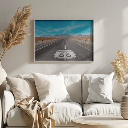 A framed photograph of the iconic Historic US Route 66 shield painted on a long, straight asphalt road that stretches through a desert landscape toward distant snow-capped mountains under a vibrant blue sky. Wall Art