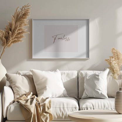 A framed artwork featuring the word 'Fearless' in a flowing brown script font on a pale pink background. The piece is surrounded by a white mat and a textured silver frame. Wall Art
