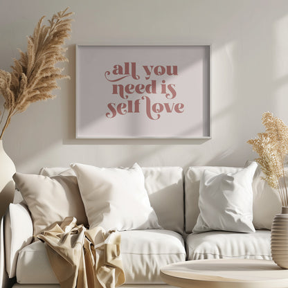 A framed art print with the phrase 'all you need is self love' in a stylish, dusty rose serif font on a light pink background. The artwork is enclosed in a simple silver frame. Poster