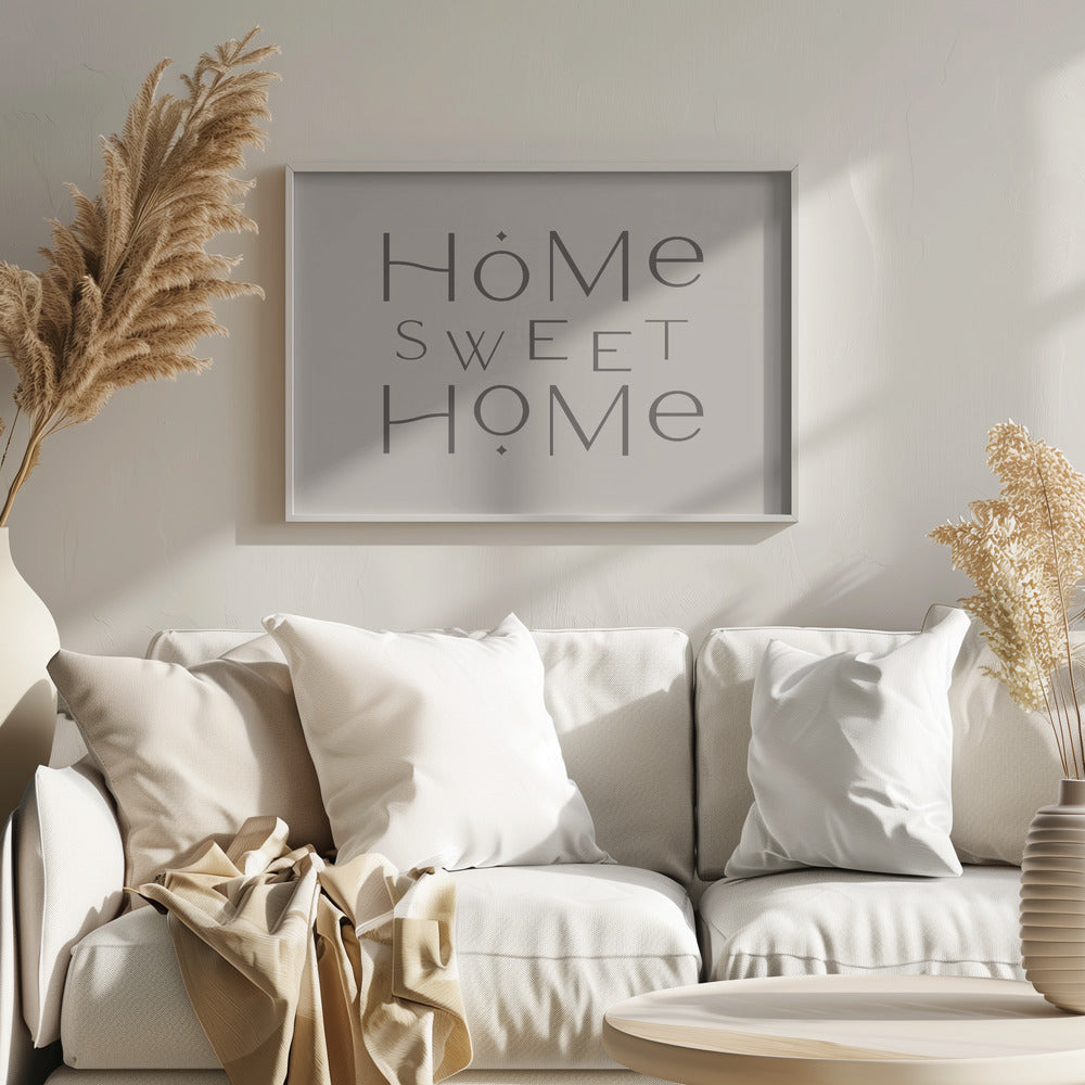 A minimalist wall art piece with the words 'Home Sweet Home' in a dark gray, stylized sans-serif font against a light beige background, all housed within a simple silver frame. Decor