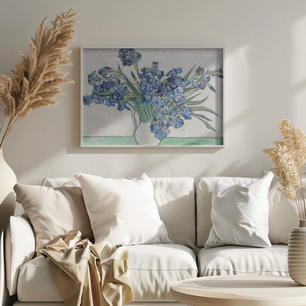 A framed print of Vincent van Gogh's famous painting 'Irises'. It features a large bouquet of vibrant blue iris flowers with long green leaves, arranged in a simple white pitcher. The background is a textured off-white wall, and the pitcher rests on a light green surface. The painting is in the post-impressionist style with thick, visible brushstrokes. Wall Art