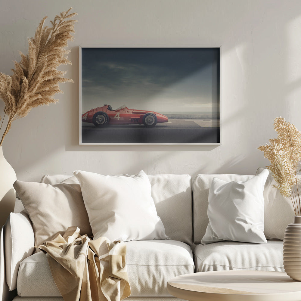 A side profile of a vintage red single-seater race car with the number 4 painted on it, parked on a seaside road under a dramatic, cloudy sky. The image has a muted, nostalgic color palette and is shown within a silver frame. Decor