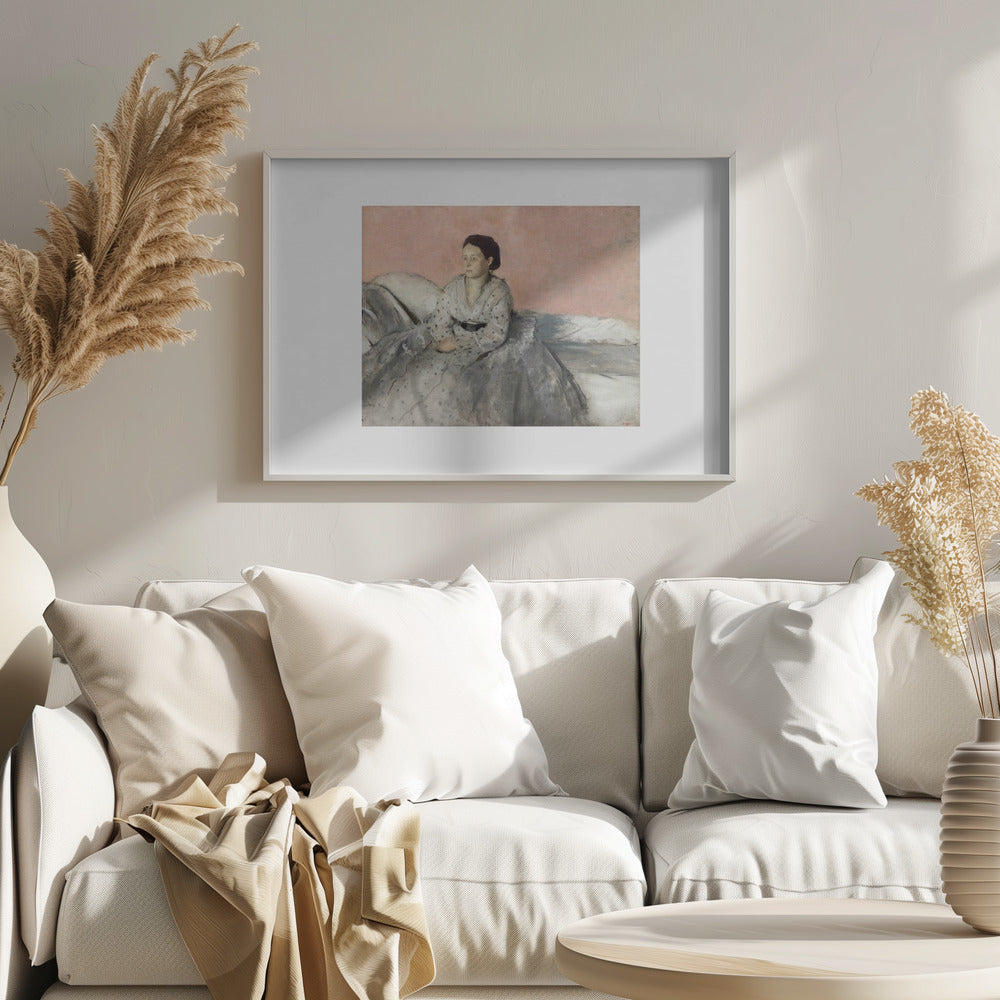 A framed impressionist painting of a woman with dark hair sitting on a bed against a dusty rose background. She wears a white, dotted blouse and a voluminous gray skirt, looking thoughtfully to her left. The painting is set in a silver frame with a white mat. Poster
