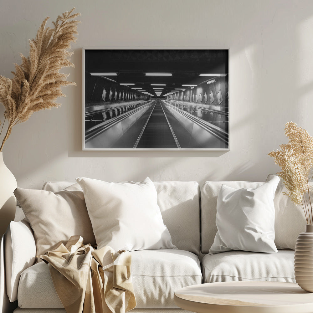 A framed, black and white, low-angle photograph looking up a long, steep, and empty escalator in a subway tunnel. The symmetrical composition uses the shiny metal handrails and rows of overhead lights as leading lines, creating a dramatic sense of depth and perspective. Print