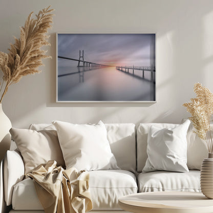 A serene long-exposure photograph of a modern cable-stayed bridge and a pier stretching over mirror-like water at sunset. The sky is filled with soft, streaky clouds in hues of pink and purple, reflected on the calm water's surface, all enclosed in a silver frame. Decor