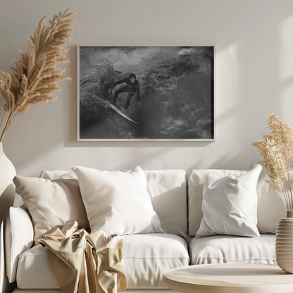 A dramatic black and white photograph of a surfer in a wetsuit skillfully riding down the face of a large, turbulent wave. The image is enclosed in a silver frame. Wall Art