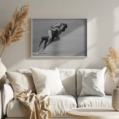 A framed, black and white photograph capturing a dynamic and romantic moment. A man is leaping off a diving board, carrying a woman who is wrapped around him in a passionate embrace, their faces close together. The background is a simple, plain gray, emphasizing their mid-air pose. Wall Art