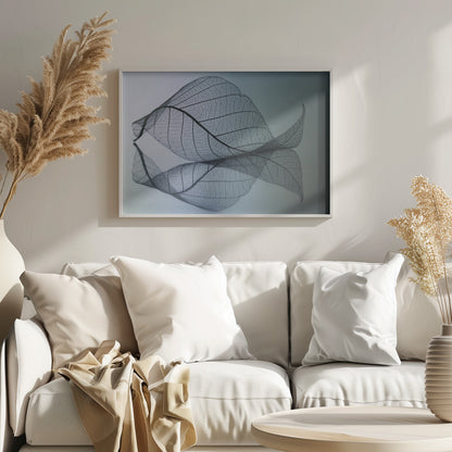 A close-up, macro photograph of a delicate skeleton leaf with intricate veins. The leaf is curled and resting on a reflective surface, creating a mirror image below it. The background is a soft, cool gradient from light blue to a darker muted teal. The image is presented within a brushed silver frame. Artwork