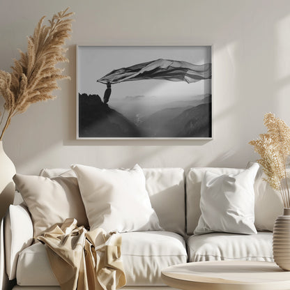 A dramatic black and white photograph of a woman standing on the edge of a mountain peak. She holds up a massive piece of dark, sheer fabric that billows in the wind, stretching across the sky. Below her, a vast, misty mountain range and a deep valley with city lights are visible. Wall Art
