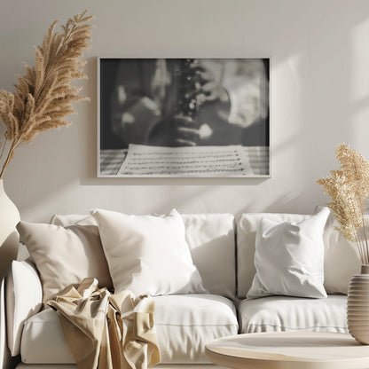 A shallow depth of field, black and white photograph focusing on sheet music in the foreground. The background is softly blurred, showing the hands of a musician holding a woodwind instrument. Wall Art