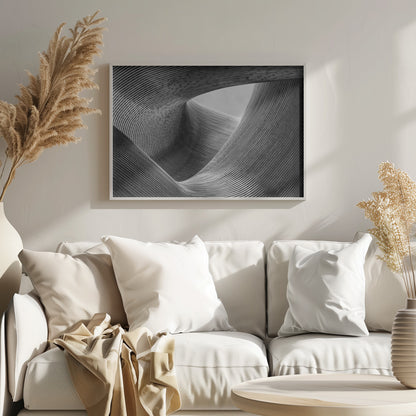 A framed, black and white abstract photograph of a swirling, textured structure. The low-angle shot looks up at curving walls made of thin, parallel lines, creating a dynamic sense of movement and depth, with an opening to a bright sky at the top. Artwork