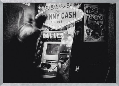 A grainy, black and white photograph of a person blurred by motion standing in front of a Johnny Cash themed slot machine. A lit marquee sign above the machine reads "HELLO I'm JOHNNY CASH OLÉ OLÉ". The setting appears to be a dark bar or casino. Wall Art