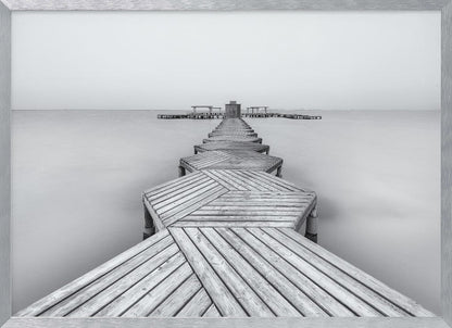 A framed, black and white photograph capturing a long wooden pier from a first-person perspective. The pier, constructed from a series of hexagonal platforms, stretches out into a calm, placid body of water that disappears into a foggy horizon, creating a serene and minimalist scene. Print